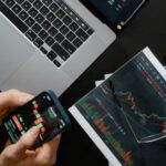Volatility In Cryptocurrency Trading - Hands Holding a Smartphone with Data on Screen