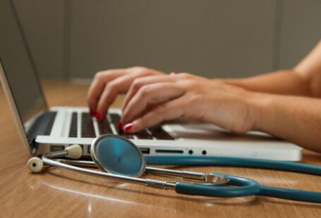 Healthcare - person sitting while using laptop computer and green stethoscope near